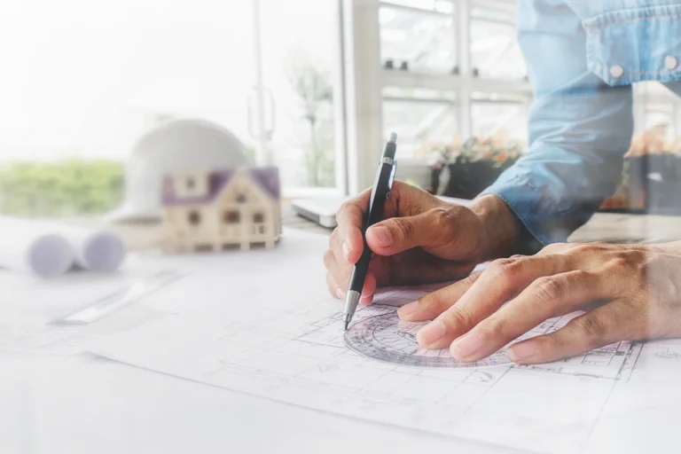 Arquitecto dibujando un plano junto a la maqueta de una vivienda