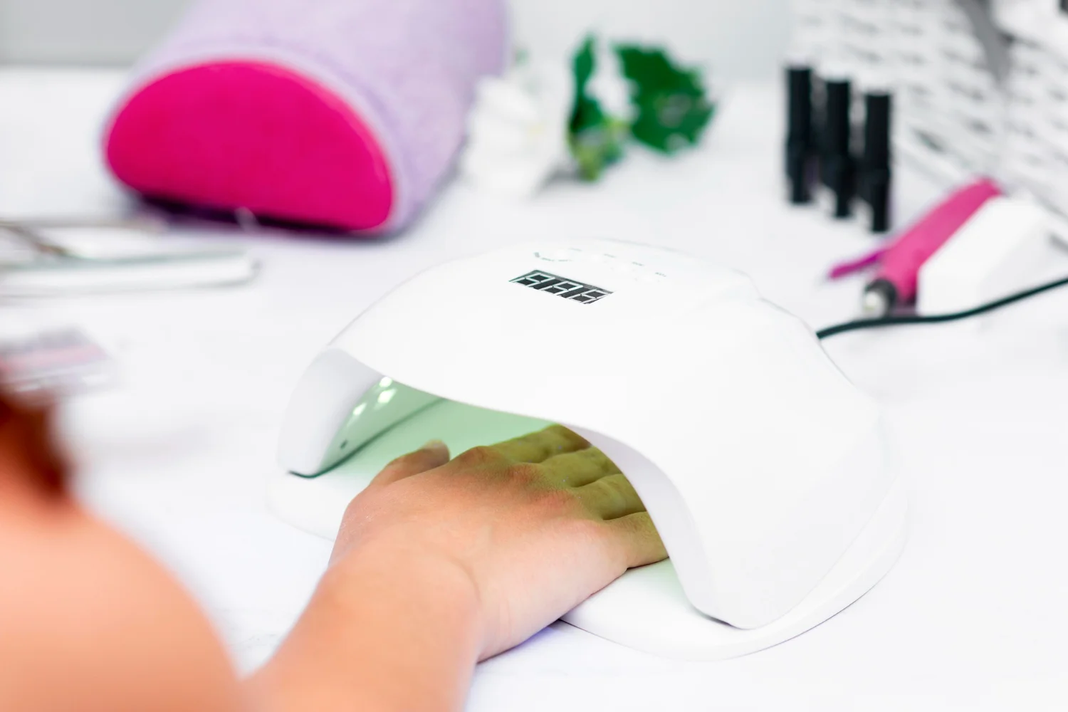 Mano introducida en una lámpara UV LED blanca para el curado de esmalte semipermanente de uñas en una mesa de manicura