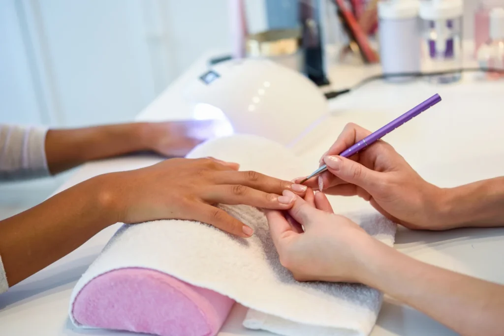 Manicurista aplicando con pincel una capa fina de esmalte semipermanente sobre la uña de una clienta
