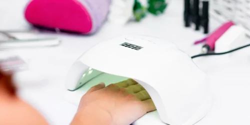 Mano introducida en una lámpara UV LED blanca para el curado de esmalte semipermanente de uñas en una mesa de manicura